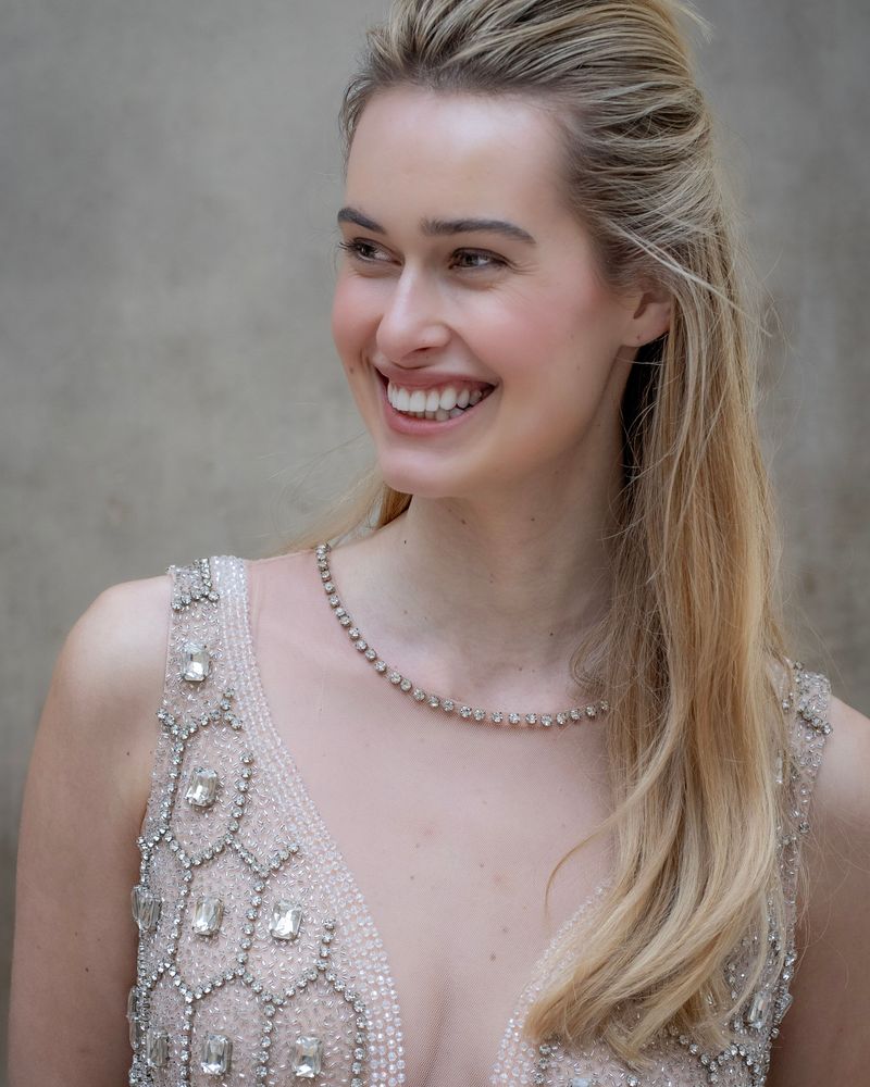 Smiling model in an intricately beaded, Art Deco-style embellished dress against a neutral background in Milan