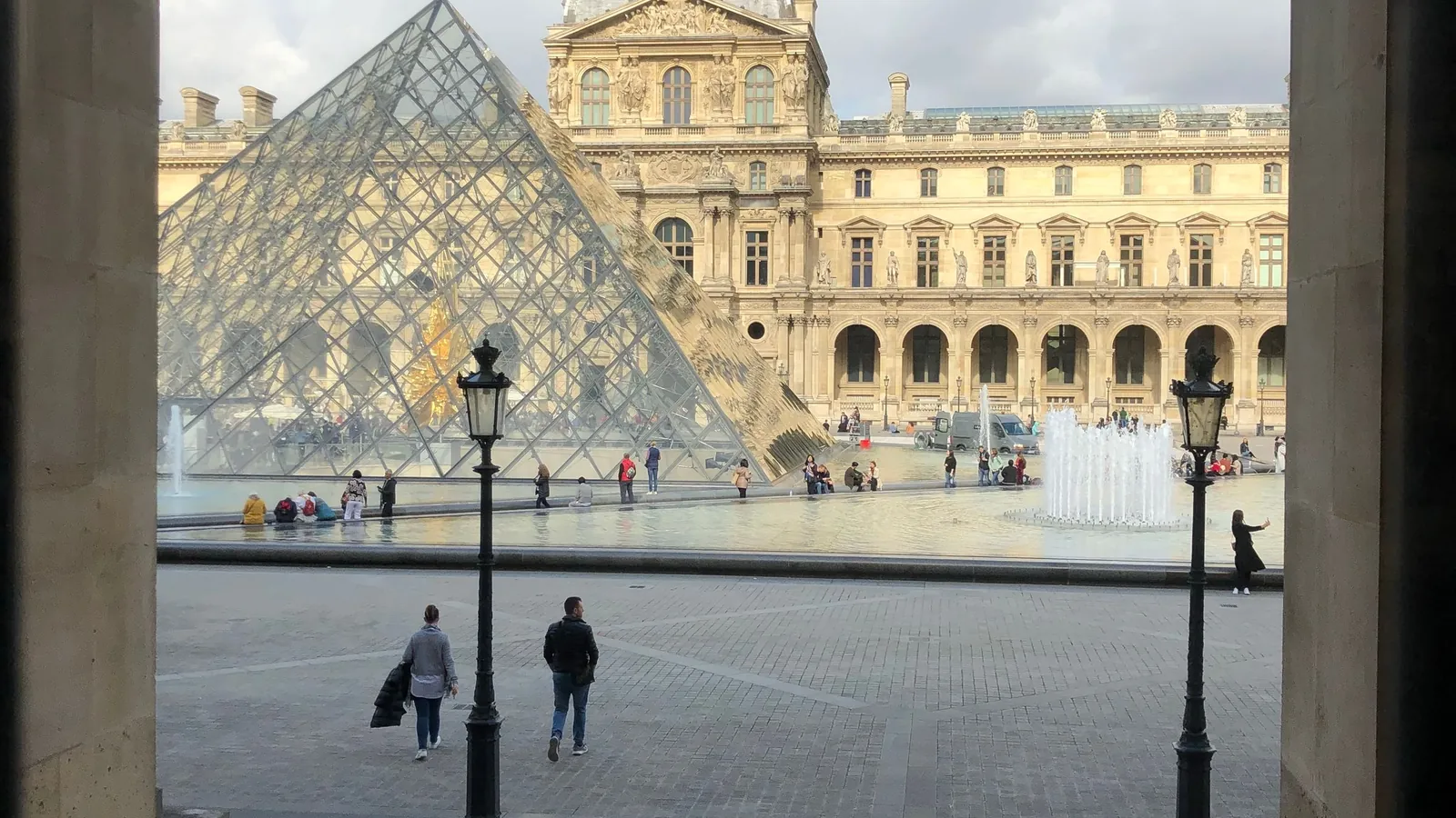 The Louvre courtyard and glass pyramid in Paris, framed by a stone archway