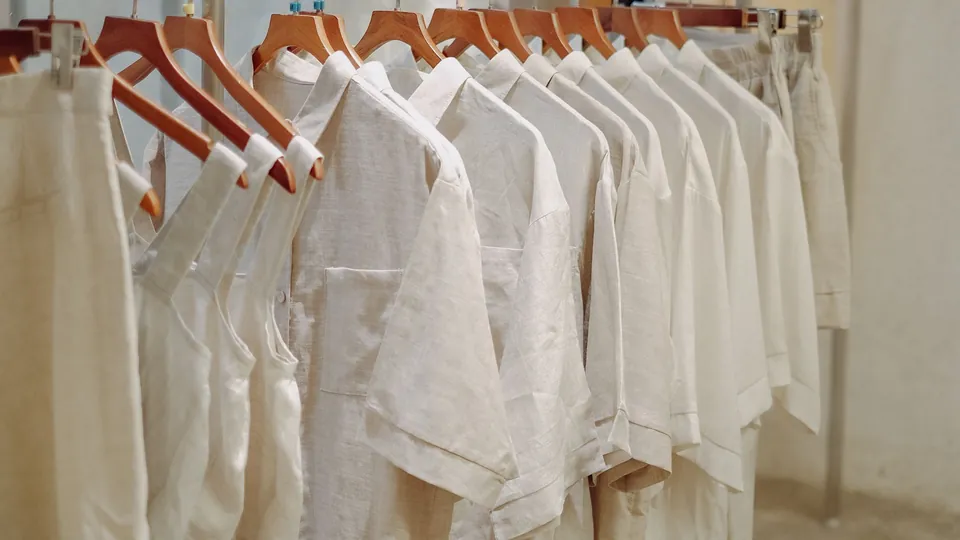 Cream and white linen shirts on wooden hangers along a minimalist clothing rail