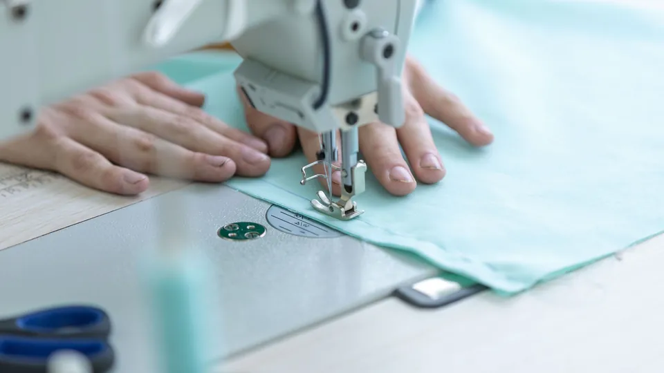 Hands guiding pale mint fabric under the needle of a sewing machine