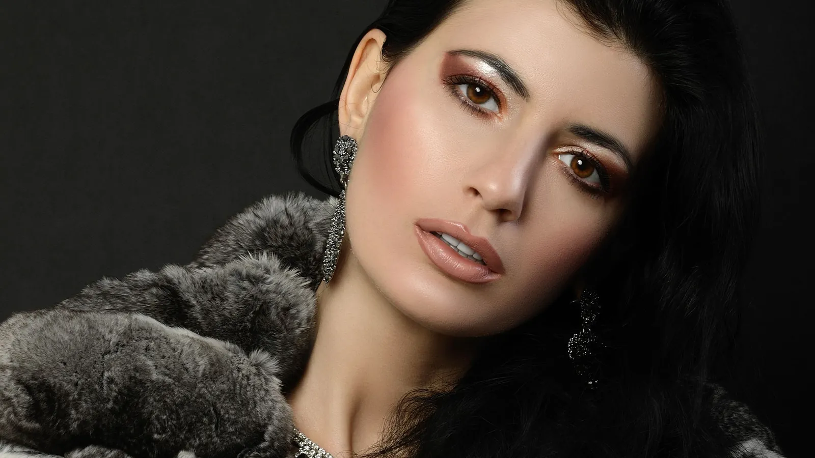 Model wrapped in a plush grey faux fur coat with a statement necklace against a dark studio backdrop