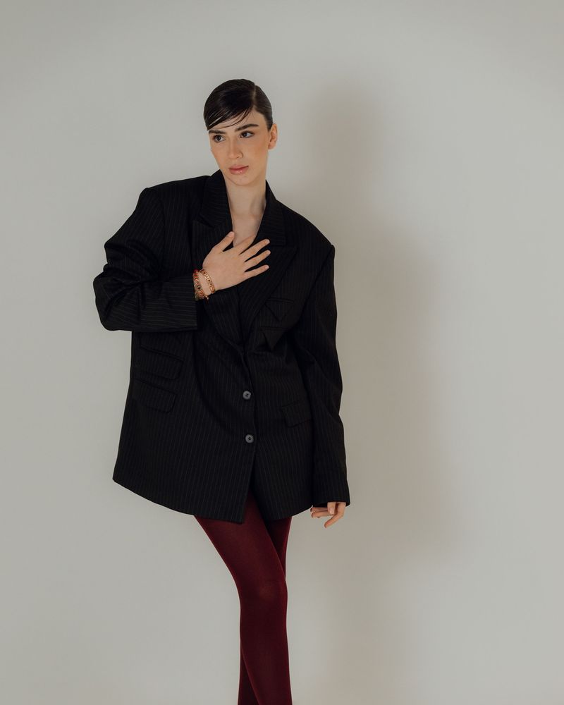 Model in an oversized black blazer with burgundy tights, posing against a neutral studio background